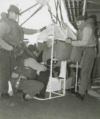Black and white photograph of enlisted men in a highline or boatswain's chair on the hangar dec…