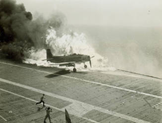 Black and white photograph of a Douglas AD-6 Skyraider engulfed in flames after a fuel tank bro…