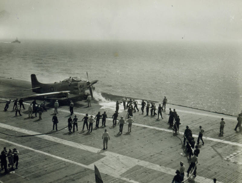 Black and white photograph of crew members putting out a fire around a Douglas AD-6 Skyraider o…