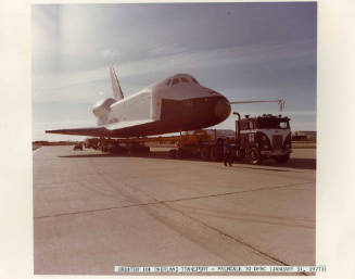 Color photograph of Enterprise arriving on tarmac of Dryden Flight Research Center towed by a t…