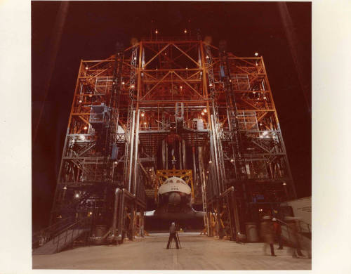 Color photograph of Enterprise being hoisted in a large orange scaffolding-like structure