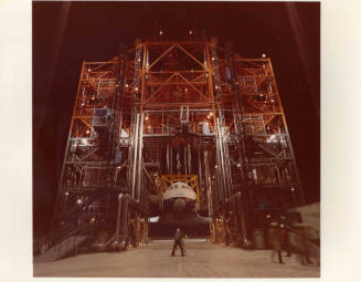 Color photograph of Enterprise being hoisted in a large orange scaffolding-like structure