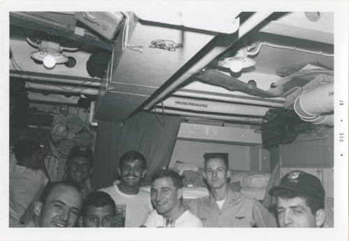 Black and white image of eight men standing inside a stateroom smiling for the camera