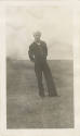 Black and white photograph of a sailor wearing a dress blue uniform and standing in a field