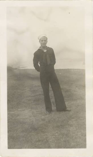 Black and white photograph of a sailor wearing a dress blue uniform and standing in a field
