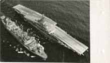 Black and white photograph of USS Intrepid sailing next to oiler ship with fuel lines between t…