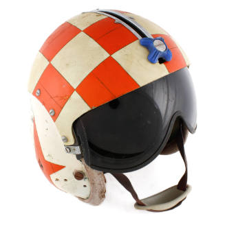 Face view of U.S. Navy flight helmet with orange and white checkerboard pattern, blue knob, bla…