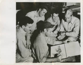 Black and white photograph of four Navy officers watching Ed Ritter draw a cartoon of an airpla…