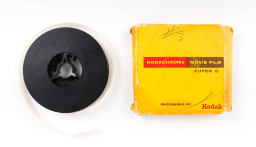 Image of black Super 8 film reel and yellow cardboard Kodak box