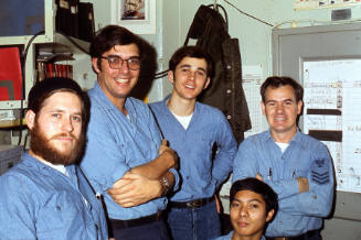 Color photograph of five photographer’s mates wearing dungarees posing in the photo lab