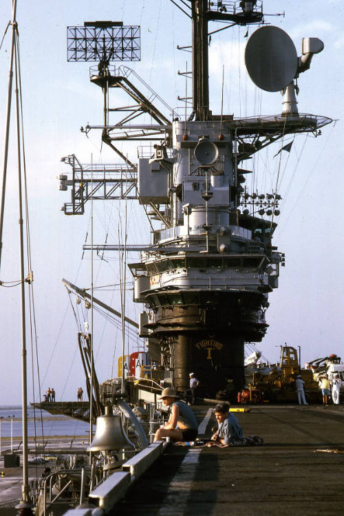 Color photograph of USS Intrepid's island with some sailors in view on the flight deck