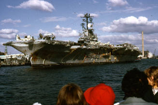 Color photograph of USS Intrepid at dock with people looking on