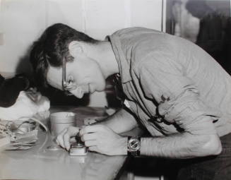 Black and white photograph of photographer's mate leaning over a table repairing a light meter