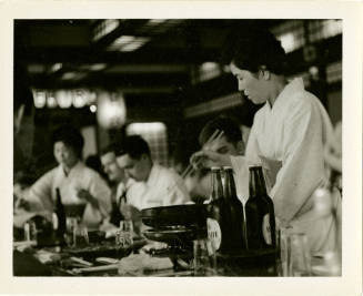 Black and white photograph of sailors in a Japanese resturant with waitresses in traditional cl…