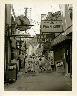 Black and white photograph of sailors in dress white uniforms walking down a street in Yokosuka…