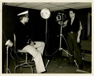 Black and white photograph of a photographer's mate taking a portrait of a seated officer