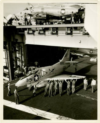 Black and white photograph of a Douglas A-4C Skyhawk on the aircraft elevator with crewmembers …