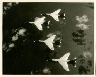 Black and white photograph looking down at four F-8 Crusaders in flight