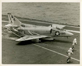 Black and white photograph of a Douglas A-4 Skyhawk crash landing into a crash barricade net wi…