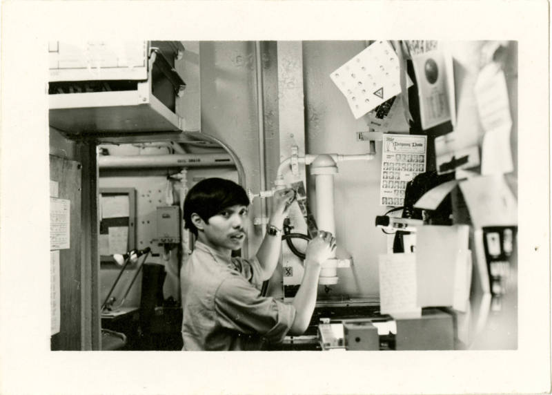 Black and white photograph of a photographer’s mate reviewing negatives in the photo lab