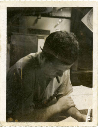 Black and white photograph of a sailor bent over a desk inside a submarine