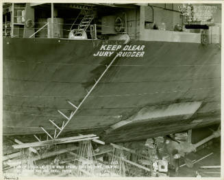 Black and white photograph of USS Intrepid in dry dock with the rig for a jury rudder visible o…