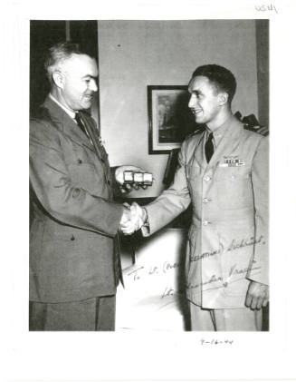 Black and white photo of Admiral McFall shaking hands with and presenting Lieutenant Vraciu wit…
