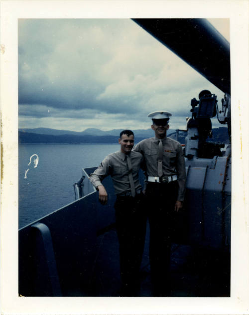 Printed color photograph of two Marines posing next to an anti-aircraft gun on a ship