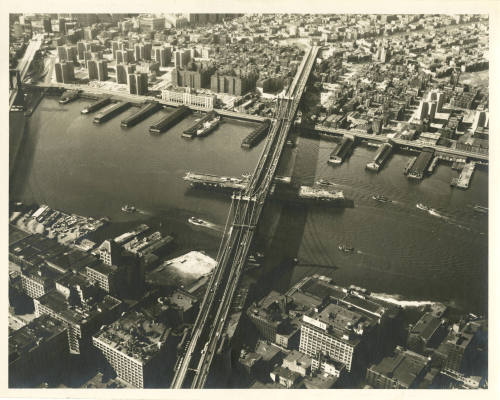 Printed black and white photograph of USS Intrepid passing under the Manhattan Bridge
