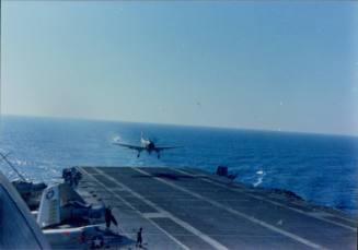 Color photograph of an aircraft landing on USS Intrepid’s fight deck