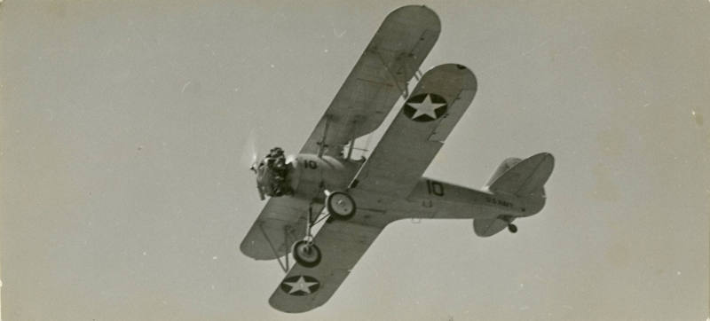 Printed black and white photograph of an aircraft in flight from below
