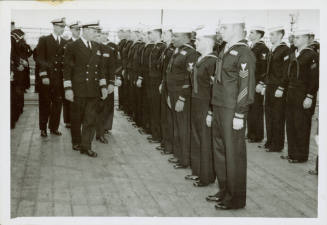 Black and white photograph of a captain inspecting sailors on USS Intrepid’s flight deck
