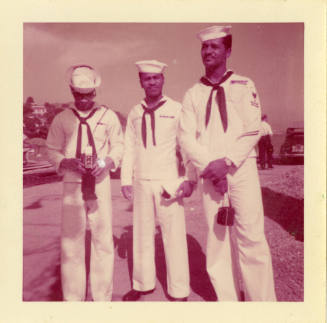 Printed color photograph of three dark skinned sailors wearing white enlisted uniforms standing…