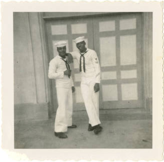 Printed black and white photograph of two enlisted sailors standing in front of a door