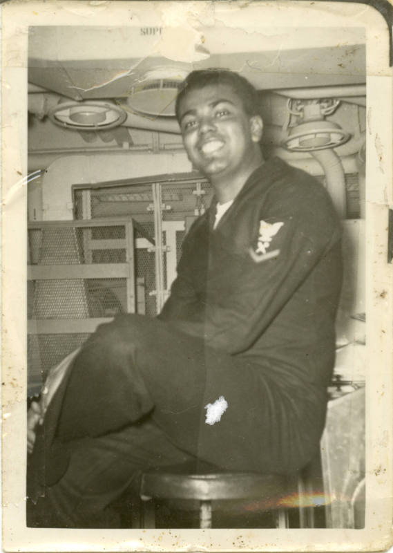 Printed black and white photograph of Navy sailor Walter Babcock sitting in a ship space