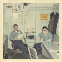 Printed color photograph of two sailors in dungaree work uniforms sitting in sick bay's adminis…