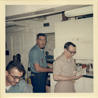 Color photograph with three crewmembers working in sick bay's treatment room