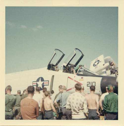 Color photograph of Intrepid crewmembers standing around an F-4 Phantom on the flight deck