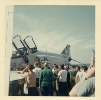 Color photograph of Intrepid crewmembers inspecting a F-4 Phantom on the flight deck