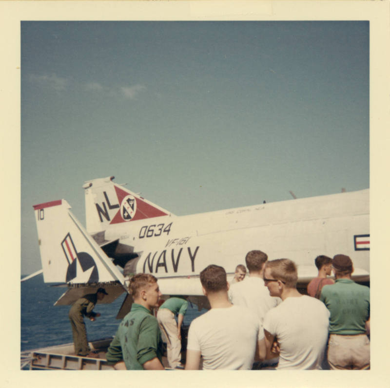 Color photograph of Intrepid crewmembers inspecting a F-4 Phantom on the flight deck