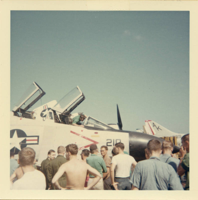Color photograph of Intrepid crewmembers surrounding a F-4 Phantom on the flight deck