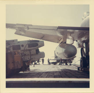 Color photograph of ordnance on the flight deck under the wing of an aircraft