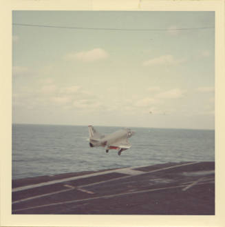 Color photograph of an A-4 Skyhawk above Intrepid's flight deck