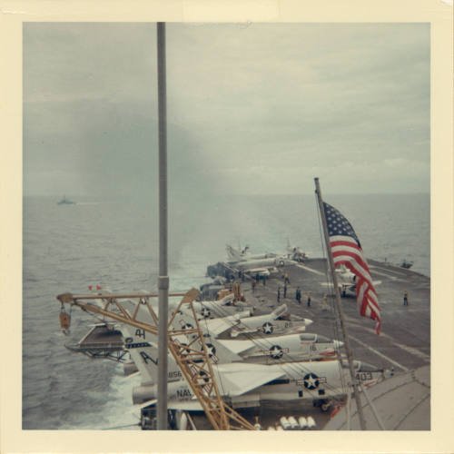 Color photograph of an aicraft landing on Intrepid's flight deck with other aircraft lined up