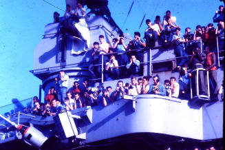 Digital color photograph of USS Intrepid crewmembers on the island looking down onto the flight…