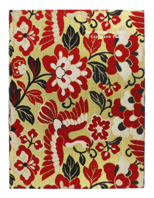Front cover of fabric covered cruise book with gold background and red, white and green floral …