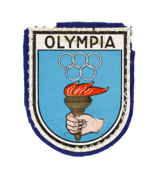 Shield shaped patch with blue felt backing and colored image of Olympic rings and torch