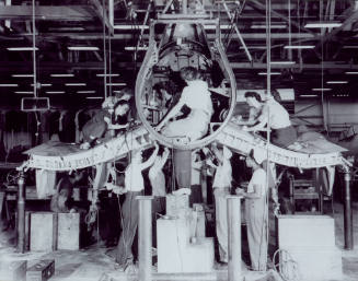 Printed black and white photograph of women working on an aircraft, possibly a Vought F4U Corsa…