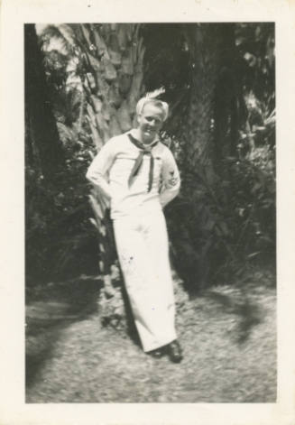 Printed black and white photograph of sailor Byron B. Joslin leaning against a tree and smiling…