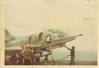 Printed color photograph of a Douglas A-4 Skyhawk on Intrepid's flight deck with flight deck pe…